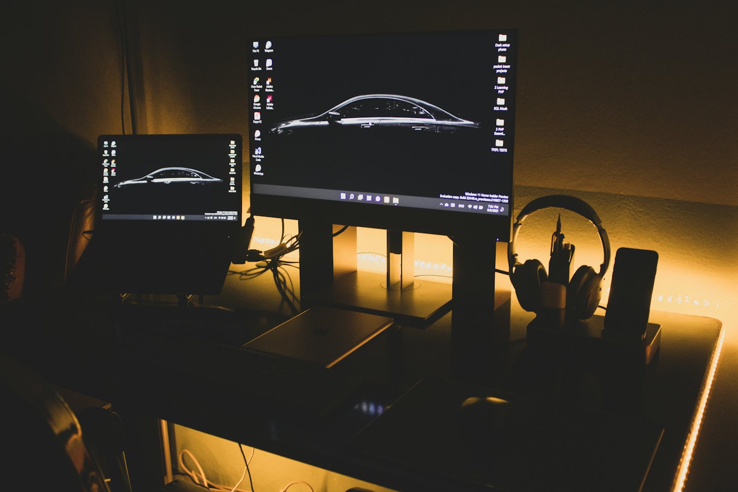 Laptop and monitor on a modern desk displaying car wallpaper.